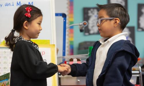 Boy and girl shaking hands in kindergarten classroom