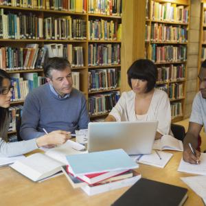 Four adults sitting at a library table looking at a laptop.