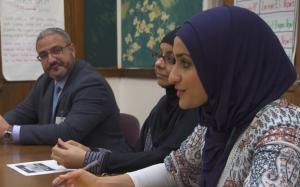 three people sitting at a table. one woman is in a hijab.