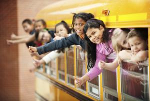 children waving from the windows of a school bus