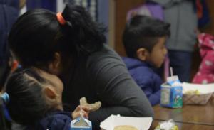 children eating. one adult sits with them.