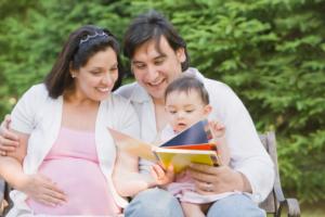 A pregnant woman, a man, and a baby all looking at a book