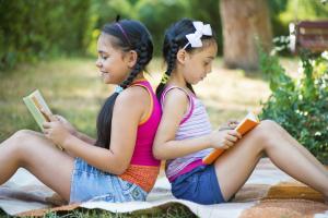 Two young girls sitting back-to-back and reading