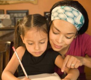 A young girl writes while a woman looks over her shoulder
