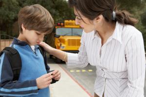 A woman talking to a sad boy in front of a school bus.