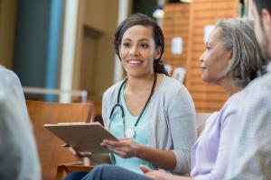 A woman with a stephoscope and clipboard is smiling at a group of adults.