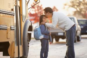 Father kissing daughter near school bus