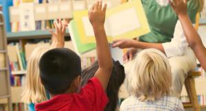 Children raising their hands in class as someone reads to them.