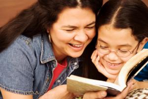 A smiling mother and daughter reading together.