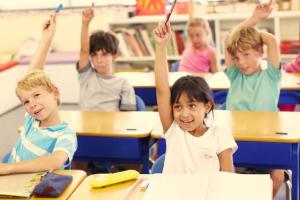 A classroom of children raising their hands.