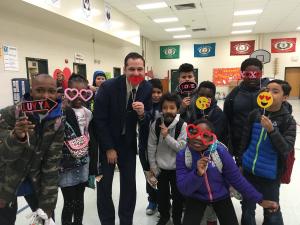 One adult and a group of kids holding up silly masks to their faces, like emojis, hearts and lips.