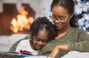 Young girl reading with mom near fireplace