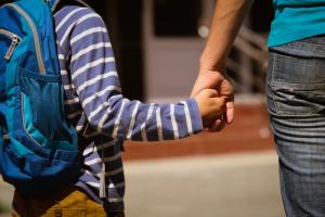 a child wearing a backback holding an adult's hand