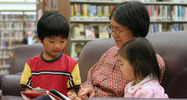 an adult and two children sitting in a library looking at a book