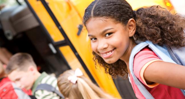 girl smiling at the camera as she gets on a school bus