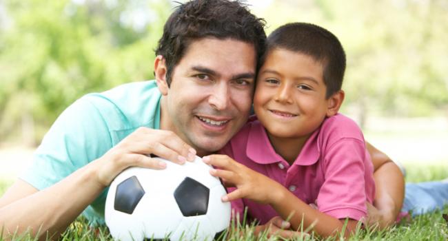 boy and man laying in the grass holding a soccer ball