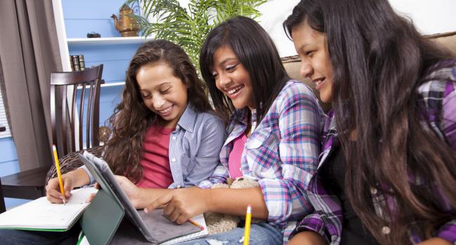 Three girls smiling as they do work on a tablet computer
